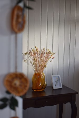 Kompozycja z suszonych kwiatów i traw w bursztynowym wazonie na drewnianym stoliku, aranżacja boho